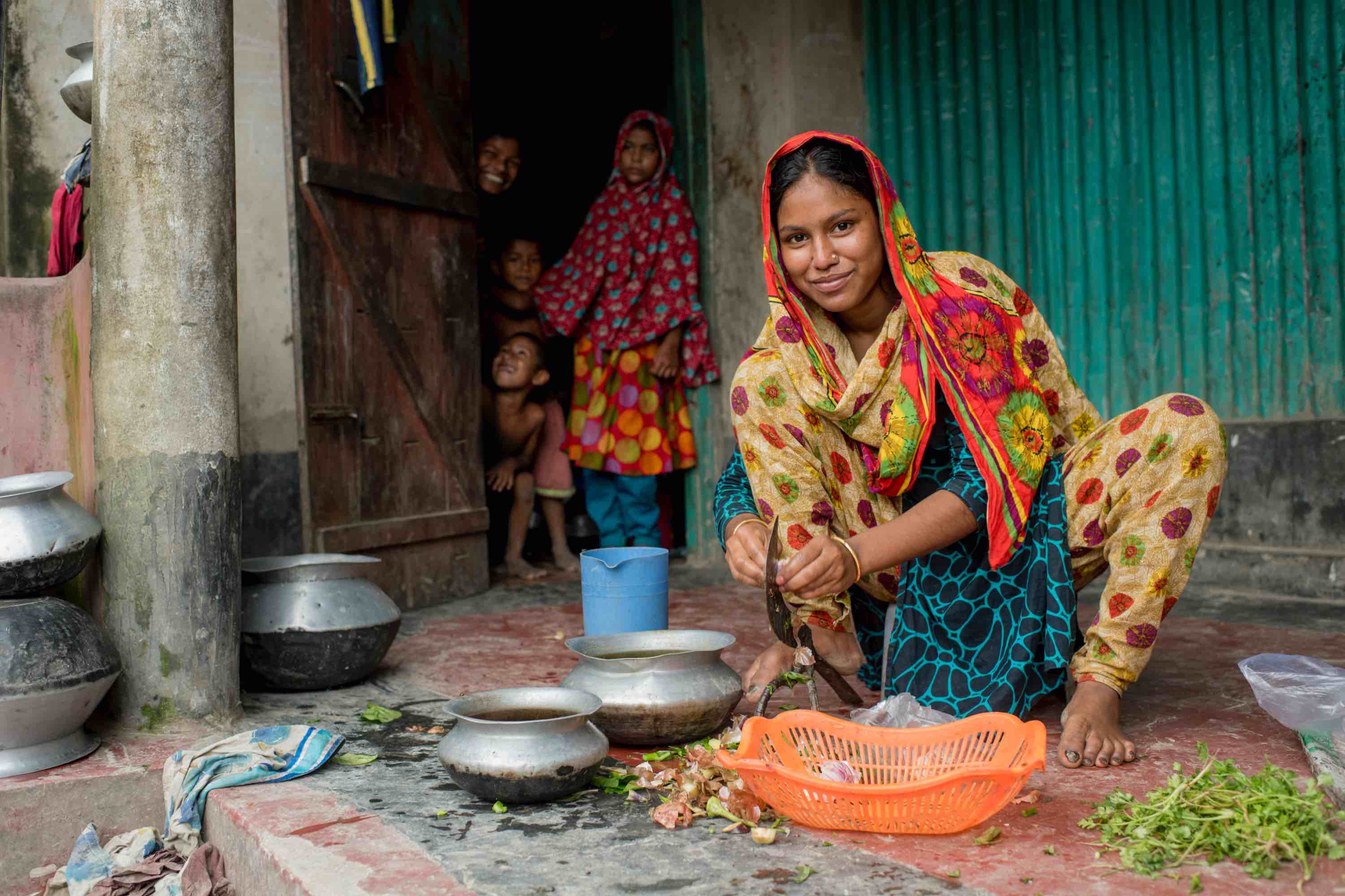 A Bangladeshi woman smiles as she cuts vegetables. 