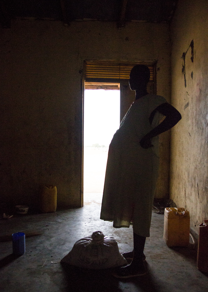 A silhouetted pregnant woman rests at an IDP site.
