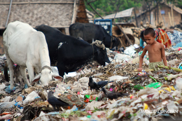 A boy wades through a festering trash pile in Bangladesh, looking for food. Humanitarian organization World Concern is working nearby, improving opportunities in the neighborhood with small business funding.