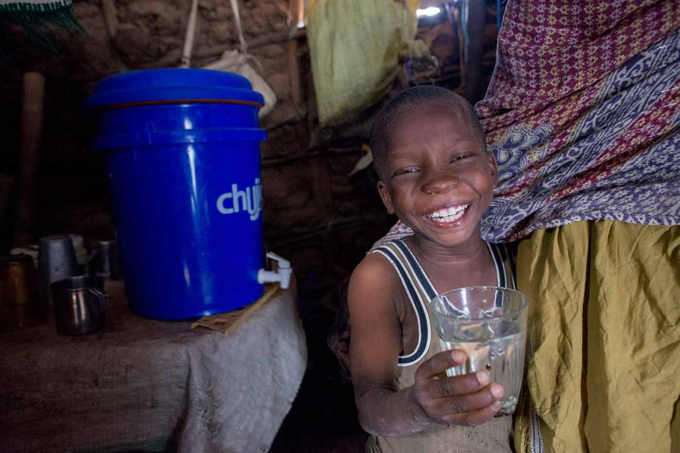 a boy smiles holding a water glass