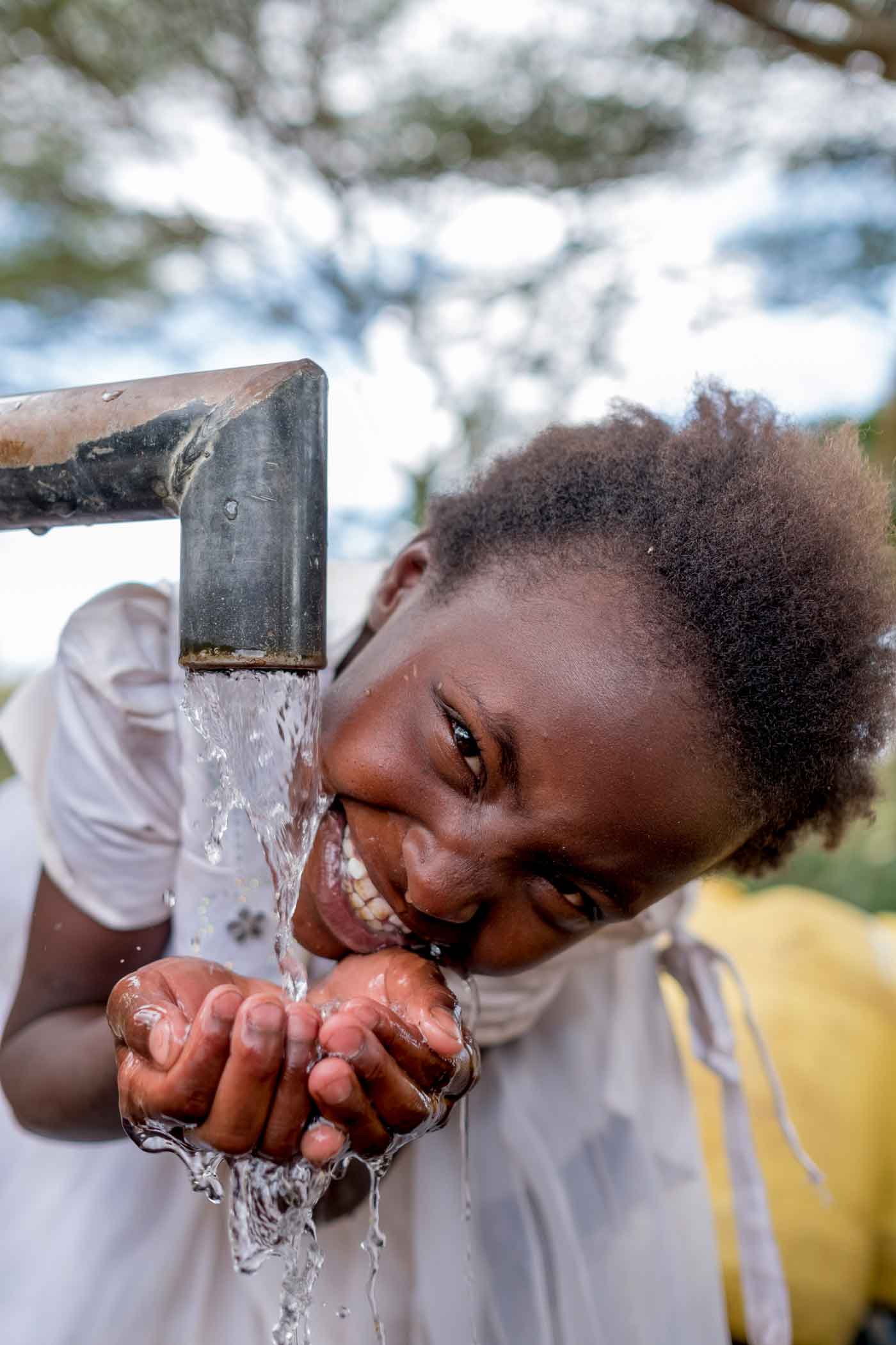 a girl in a white dress drinks from a clean water well