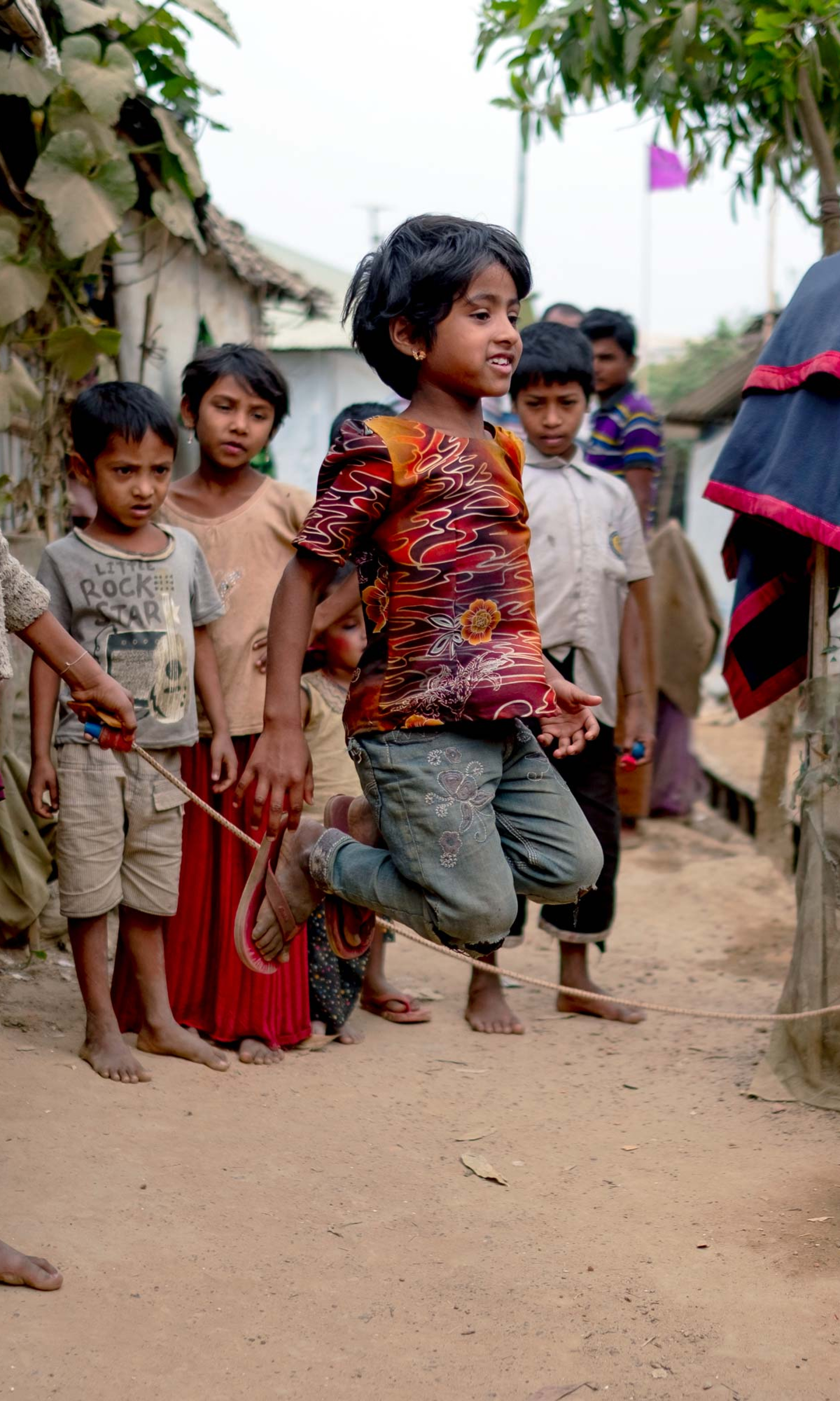 Children in gather around as three girls jump rope together.