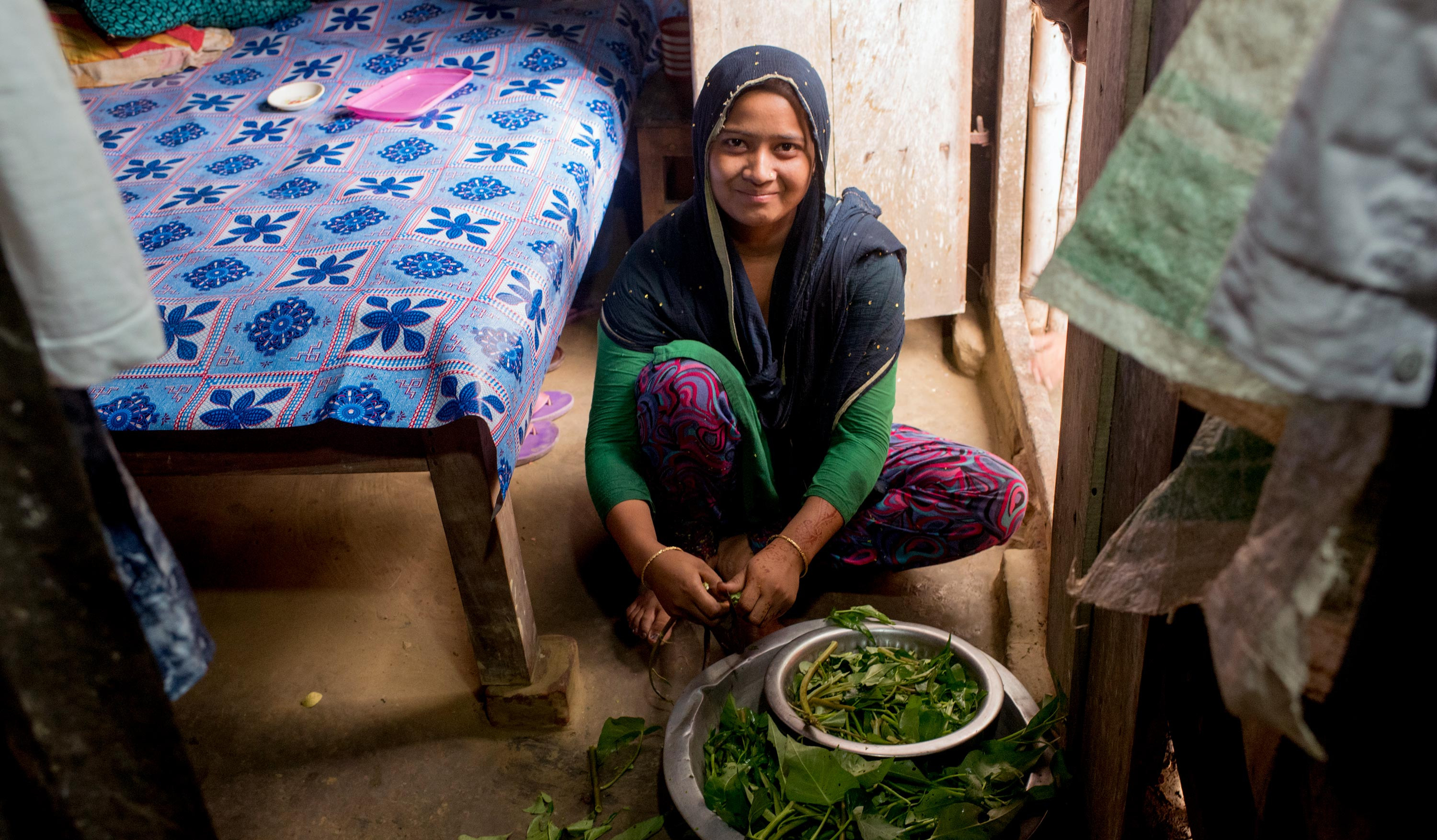 A Bangladeshi woman cuts vegetables inside her home.