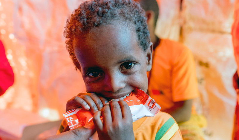 A young Somali boy eats a nutripacket full of emergency nutrition.