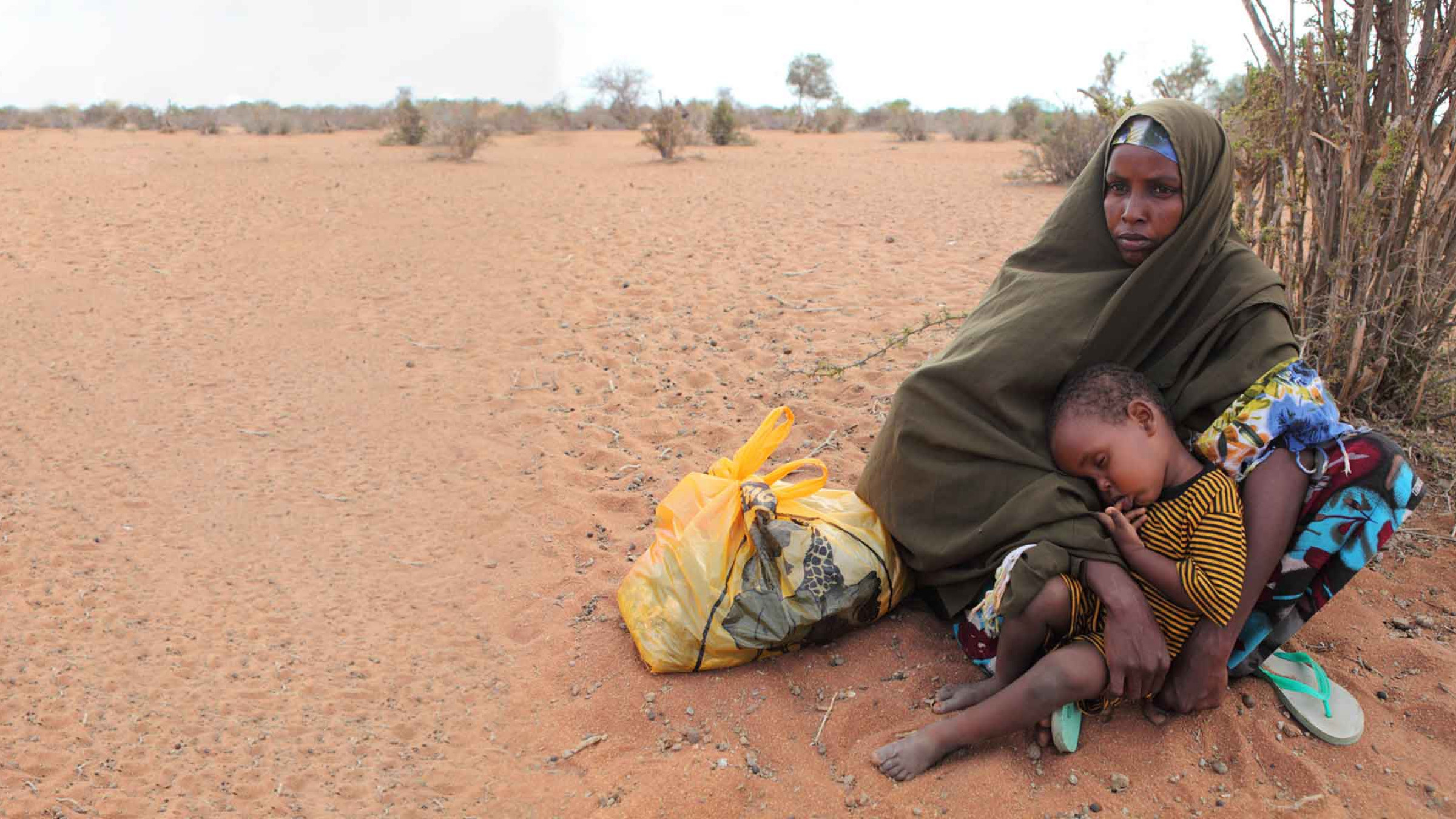 A little boy sleeps on his mother's lap as she rests on the long walk from Somalia to refugee camps in Kenya.